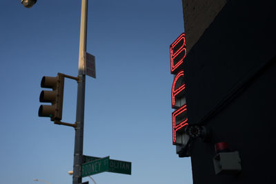 Low angle view of signal by illuminated neon red bar sign on building against sky