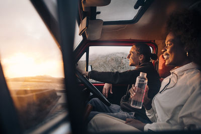 Happy woman holding water bottle while sitting with male friend driving van on vacation