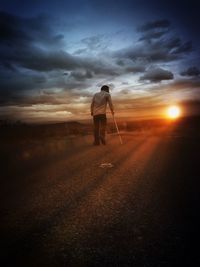 Rear view of man walking on road against sunset sky