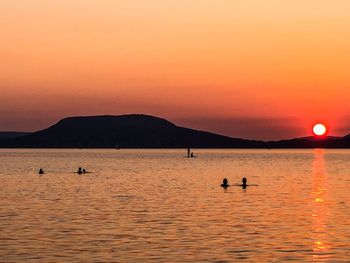 Silhouette people on sea against orange sky