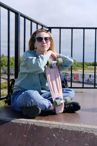 A young girl of 16-18 years old sits on a ramp in a skate park