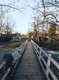 Footbridge over river amidst bare trees against sky