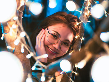 Portrait of smiling young woman by illuminated string lights