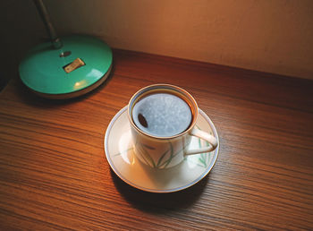 A cup of hot coffee on the table beside a lamp