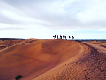 People on sand dune against sky