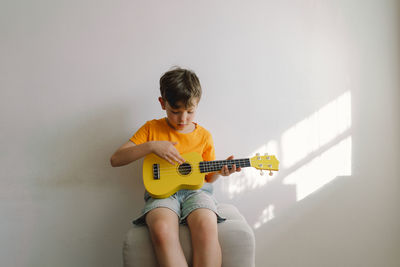 Cute boy learns to play the yellow ukulele guitar in home. cozy home.