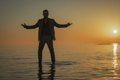 Full length of man standing in sea against sky during sunset