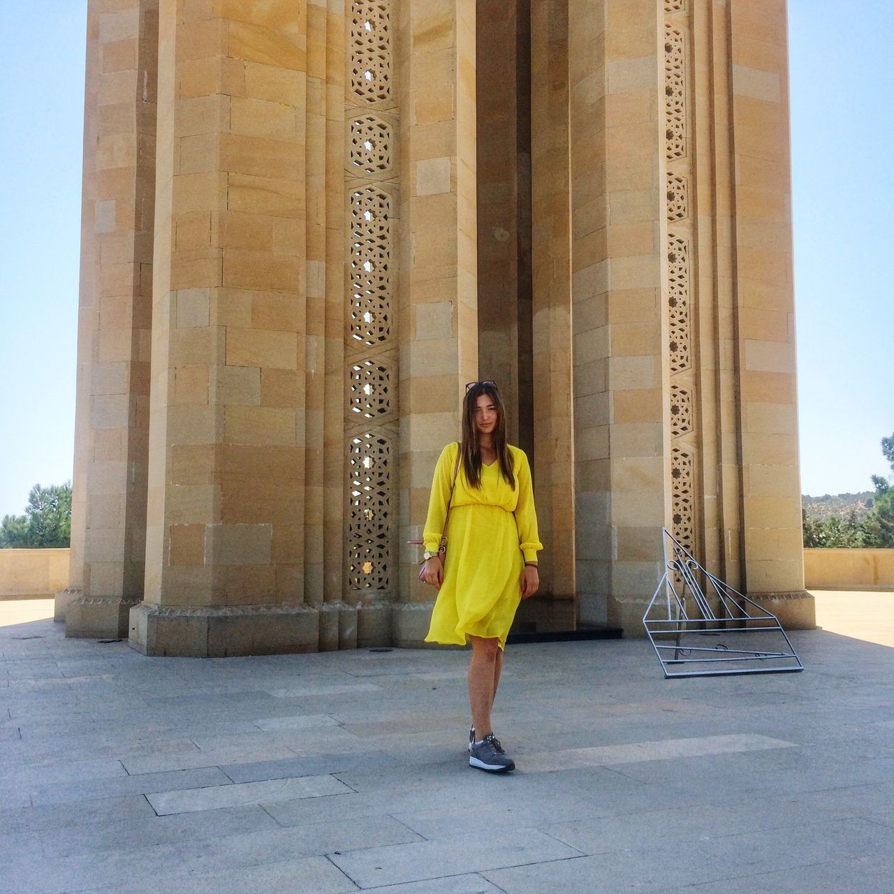 full length, young adult, architecture, lifestyles, young women, casual clothing, person, portrait, leisure activity, built structure, front view, looking at camera, smiling, building exterior, standing, column, outdoors, day, confidence, architectural column