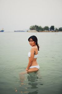 Portrait of young woman in water against sky