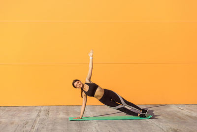 Full length of young woman with arms raised against wall