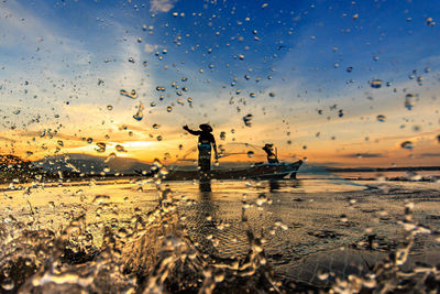 Silhouette fisherman fishing in sea against sky during sunrise