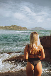 Rear view of young woman standing at beach against sky