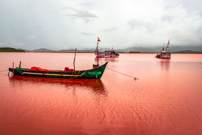 Fishing boats moored in sea against sky