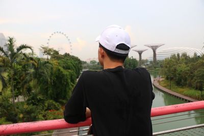 Rear view of man looking at gardens by the bay while standing on bridge