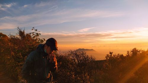 Man standing by tree against sky during sunset