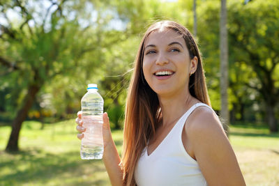 Smilingwoman have a break from work out holding a bottle of water to drink looking away in city park