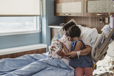 Wide view of mother holding newborn son meeting siblings