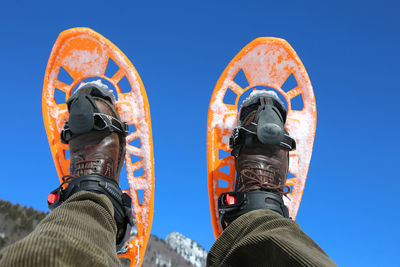 Low section of person wearing snowshoe against clear blue sky
