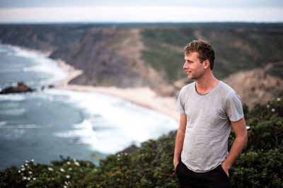 Smiling young man standing on mountain against sea