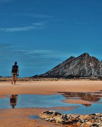 Rear view of man walking at beach against blue sky