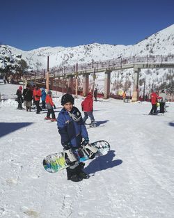 Boy sitting on snowy field against sky