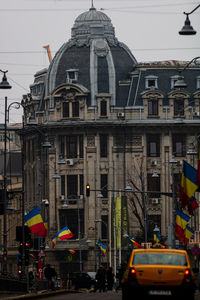 Cars on street by buildings in city against sky