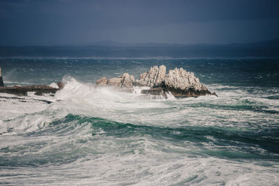 Waves splashing on shore against sky