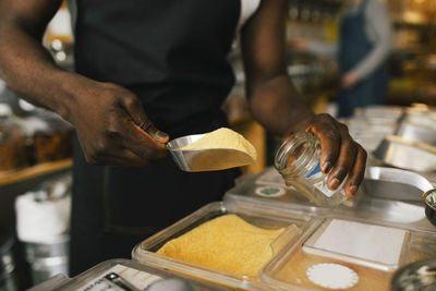 Midsection of store owner filling food in jar