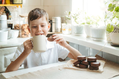 A boy is drinking milk and chocolate chip cookies in his home kitchen. happy child drinks milk 