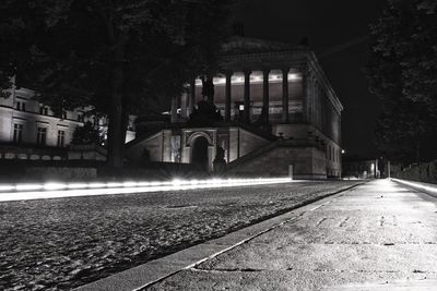 View of railroad tracks by street and buildings at night
