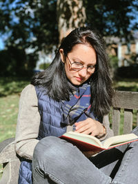 Young woman is reading red book in a park. young candid millennial woman in casual autumnal clothes 