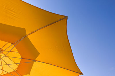 Low angle view of yellow umbrella against clear blue sky