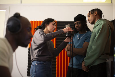 Woman adjusting microphone while rappers standing in studio