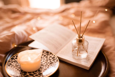 Bamboo sticks in bottle with scented candles and open book on wooden tray in bed closeup