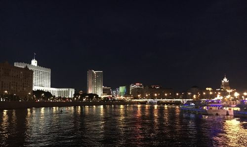 Illuminated buildings by river against sky at night