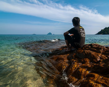 Rear view of man sitting on rock by sea