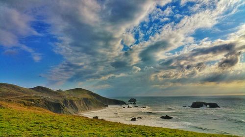 Scenic view of sea cove and cliffs against cloudy striated sky