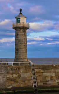 Lighthouse on sea against cloudy sky