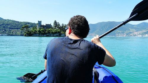 Rear view of man standing on boat in sea against sky