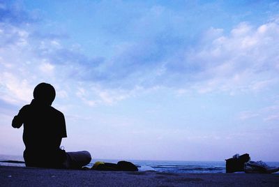 Silhouette boy sitting on beach against sky