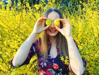 Portrait of woman holding balls against yellow flowers on field