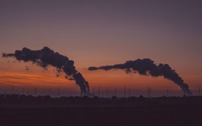 Silhouette of smoke emitting from field against sky during sunset