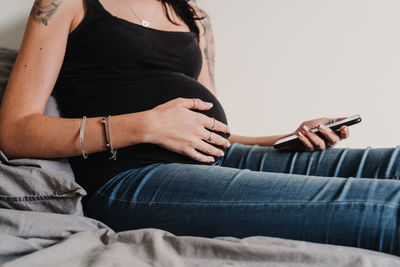 Midsection of woman using phone while sitting on bed at home