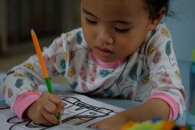 Close-up of cute girl writing with pencil on paper