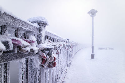 Padlocks on railing of snow covered bridge against sky