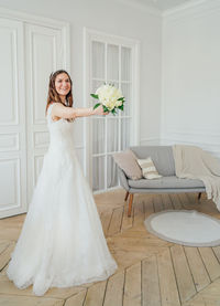 Smiling bride holding bouquet while standing at home