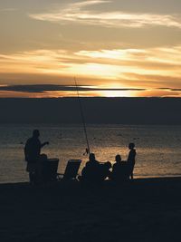 Silhouette people fishing on beach against sky during sunset