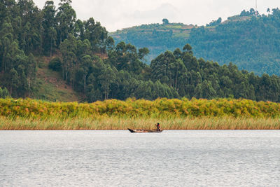 A tourist on a traditional fishing canoe at lake mutanda at sunset in kisoro town, uganda