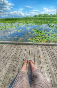 Low section of woman standing by lake against sky