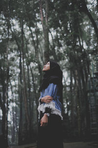 Woman standing by tree trunk in forest